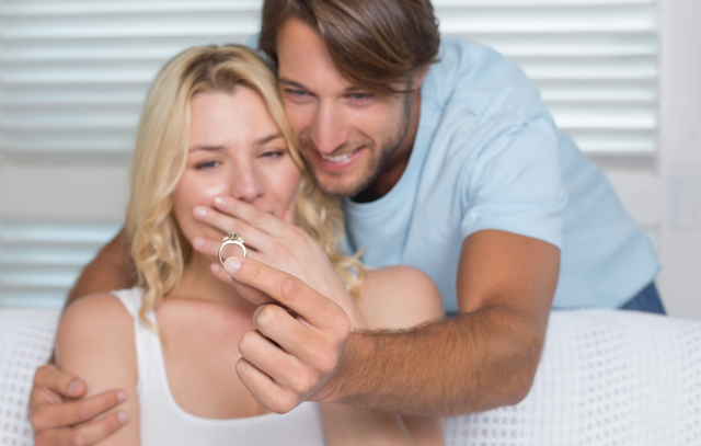 Handsome man proposing marriage to his surprised girlfriend at home in the living room