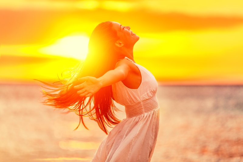 Happy woman feeling free with open arms in sunshine at beach sunset. Freedom and carefree enjoyment girl enjoying life. Beautiful woman in white dress for success, health, hope and faith concept.